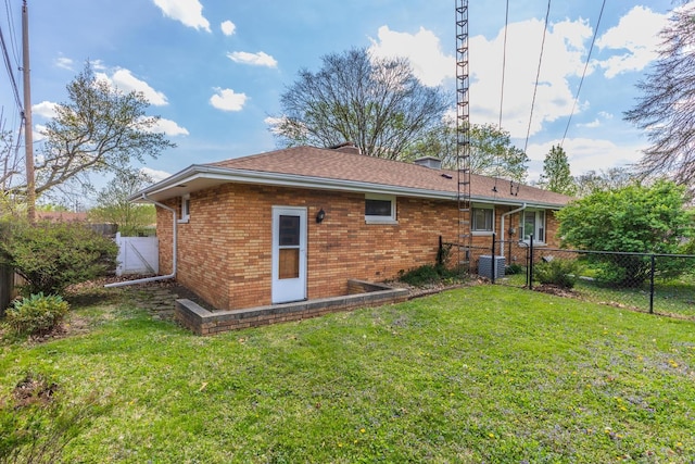 back of property featuring a lawn, central AC unit, a fenced backyard, and brick siding