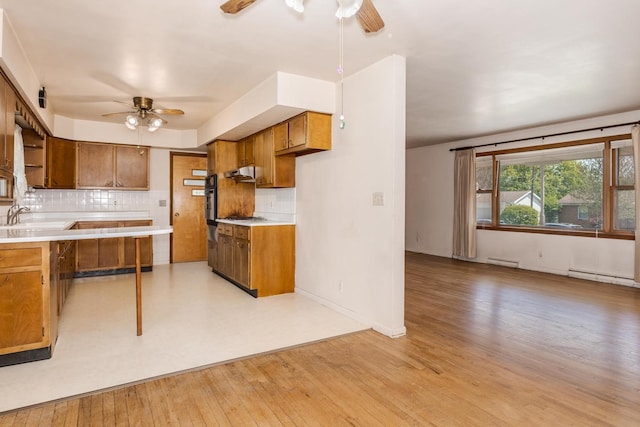 kitchen featuring decorative backsplash, under cabinet range hood, brown cabinets, a sink, and a ceiling fan