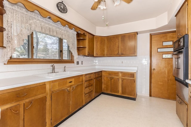 kitchen with brown cabinetry, open shelves, a sink, a ceiling fan, and stainless steel oven