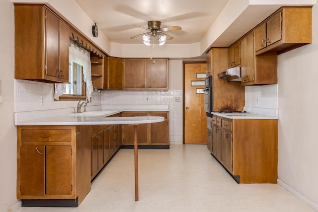 kitchen with a sink, ceiling fan, brown cabinets, and under cabinet range hood