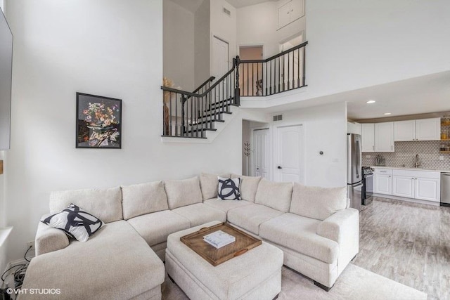 living room with light wood-type flooring, a high ceiling, stairs, and visible vents