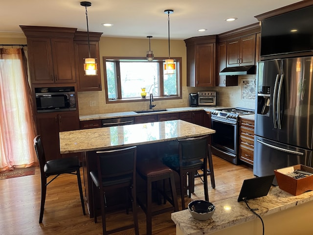 kitchen with a kitchen breakfast bar, a sink, under cabinet range hood, stainless steel appliances, and light wood-style flooring
