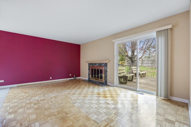 unfurnished living room with a high end fireplace, an accent wall, visible vents, and baseboards
