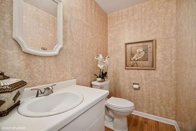 bathroom with vanity, wood finished floors, toilet, baseboards, and wallpapered walls