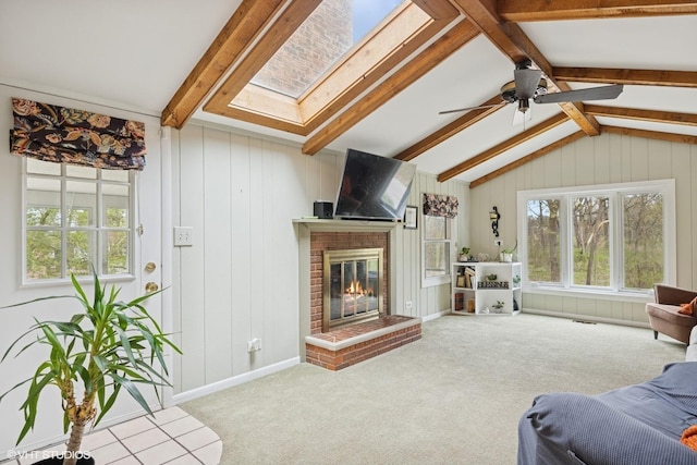 carpeted living area with a ceiling fan, visible vents, vaulted ceiling with skylight, and a fireplace