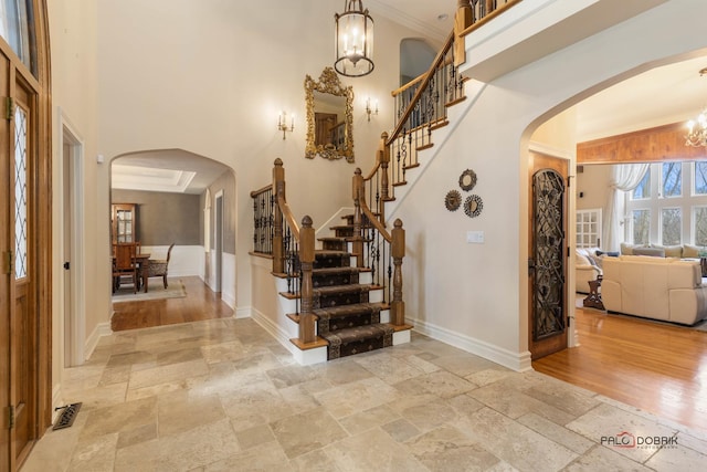 foyer entrance with a high ceiling, stone tile flooring, arched walkways, and a notable chandelier