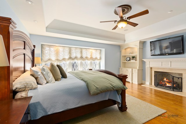 bedroom with a ceiling fan, wood finished floors, a high end fireplace, and a tray ceiling