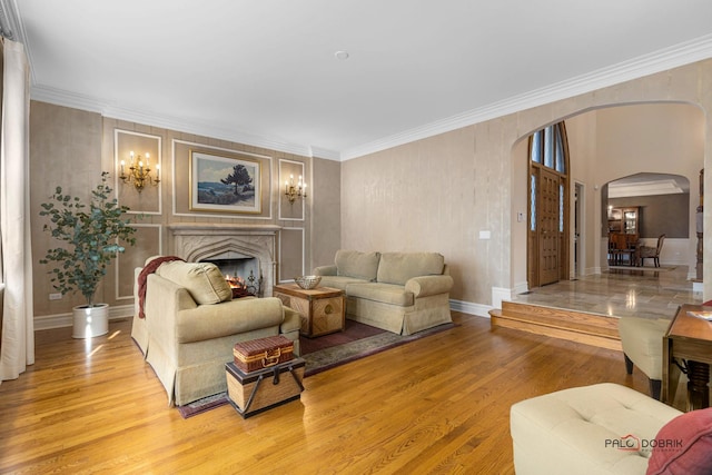 living room featuring crown molding, light wood-style floors, arched walkways, a fireplace, and baseboards