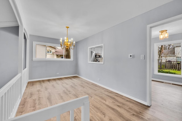 unfurnished dining area featuring baseboards, wood finished floors, a chandelier, and a healthy amount of sunlight
