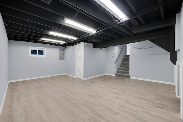 finished basement with stairway, baseboards, electric panel, and light wood-type flooring
