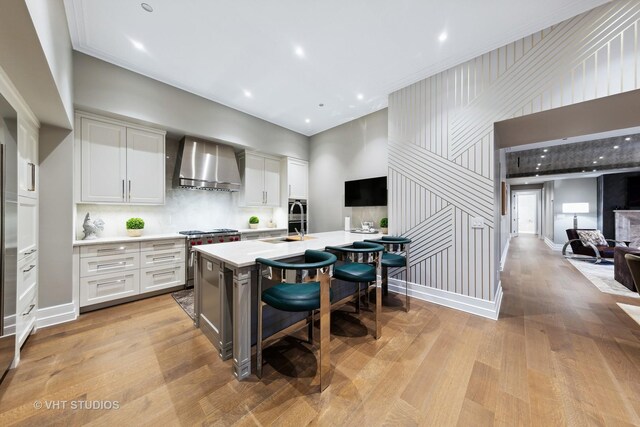 435 N Michigan Ave Unit 401, Chicago, IL 60611 - kitchen featuring light wood finished floors, light countertops, wall chimney exhaust hood, a kitchen bar, and stainless steel range