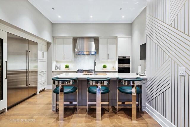 435 N Michigan Ave Unit 401, Chicago, IL 60611 - kitchen with light wood-style flooring, light countertops, wall chimney range hood, a breakfast bar, and appliances with stainless steel finishes
