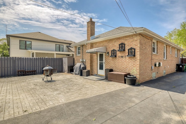 rear view of house featuring a chimney, brick siding, a patio, and fence