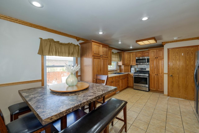 kitchen featuring stainless steel appliances, a sink, ornamental molding, brown cabinets, and light tile patterned floors