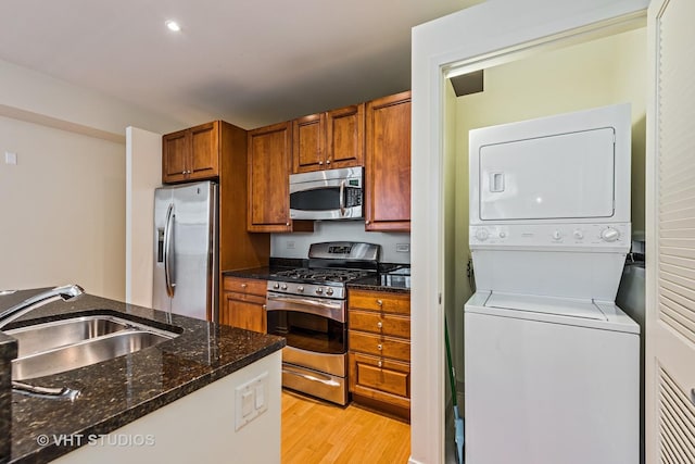 kitchen featuring appliances with stainless steel finishes, a sink, stacked washer / drying machine, brown cabinetry, and light wood-type flooring