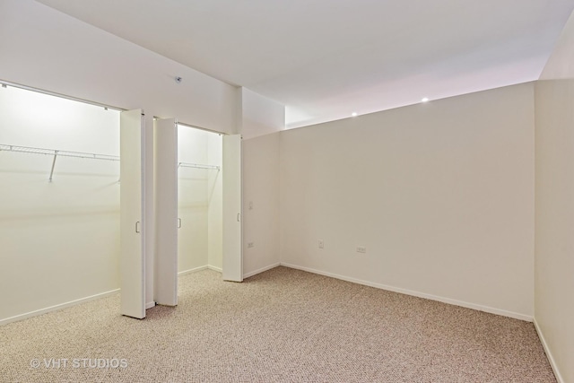 unfurnished bedroom with light carpet, multiple closets, and baseboards