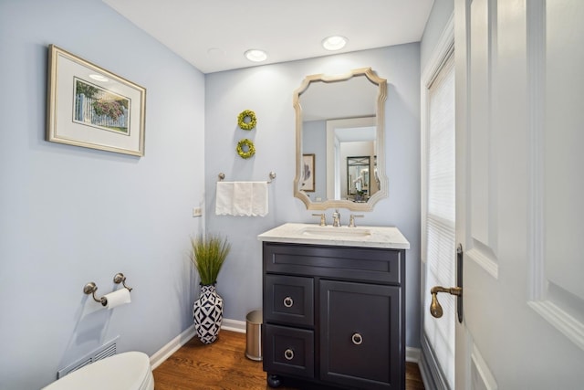 bathroom with toilet, vanity, wood finished floors, and baseboards