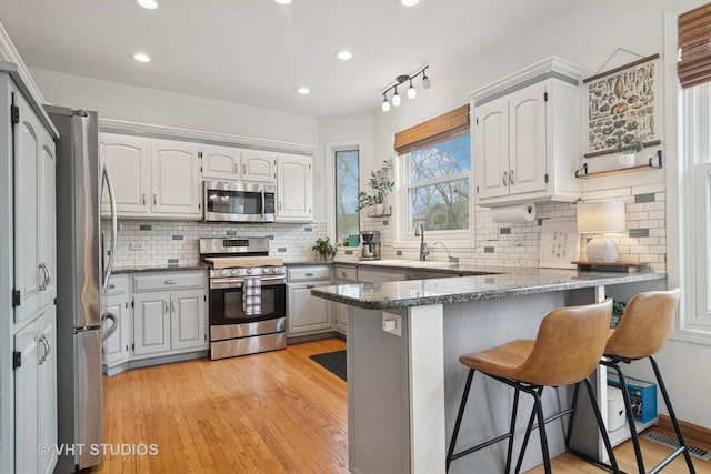 23114 W N Lakewood Ln, Lake Zurich, IL 60047 - kitchen with appliances with stainless steel finishes, a peninsula, a breakfast bar, decorative backsplash, and light wood finished floors