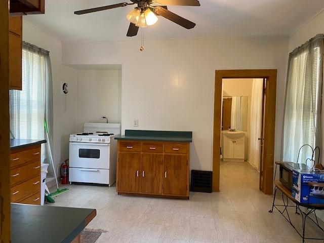 kitchen featuring light floors, white gas range, dark countertops, brown cabinetry, and ceiling fan