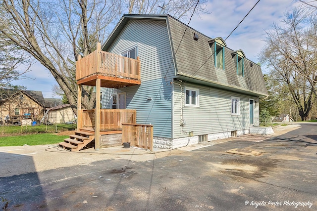exterior space with a wooden deck, a balcony, and a gambrel roof