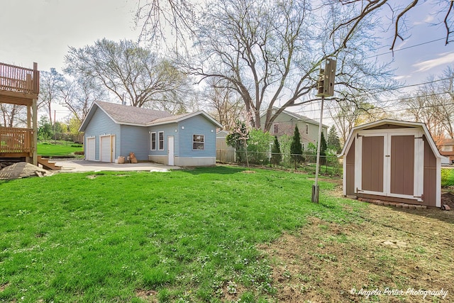 view of yard featuring fence, a detached garage, an outbuilding, and a wooden deck