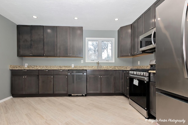 kitchen with dark brown cabinetry, recessed lighting, light stone counters, a sink, and stainless steel appliances