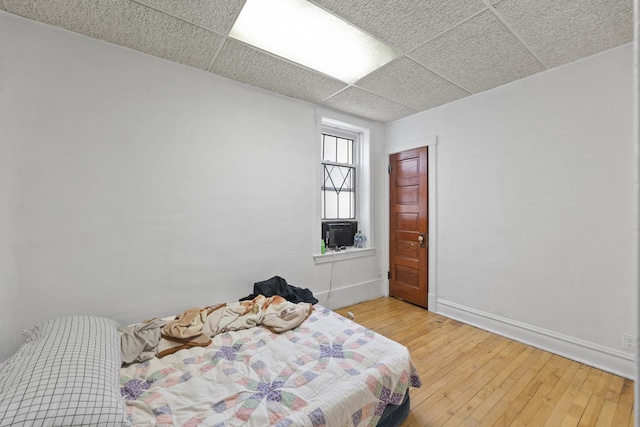 bedroom with baseboards, hardwood / wood-style floors, and a drop ceiling