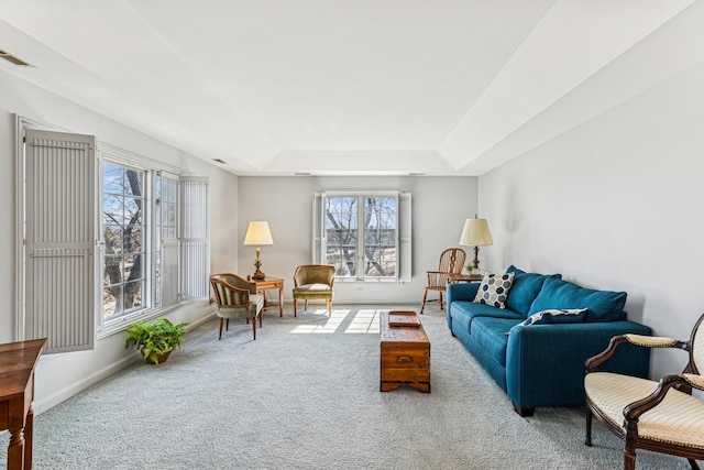 carpeted living area with visible vents, a raised ceiling, and baseboards