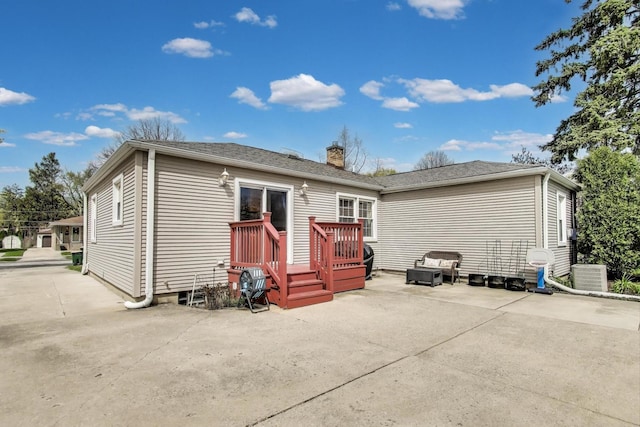 rear view of house featuring a chimney, a wooden deck, central AC unit, and a patio