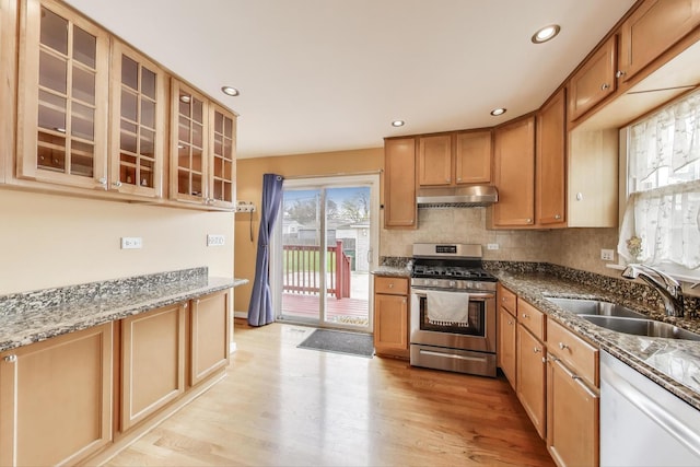 kitchen featuring white dishwasher, a sink, light wood-type flooring, under cabinet range hood, and stainless steel gas range oven