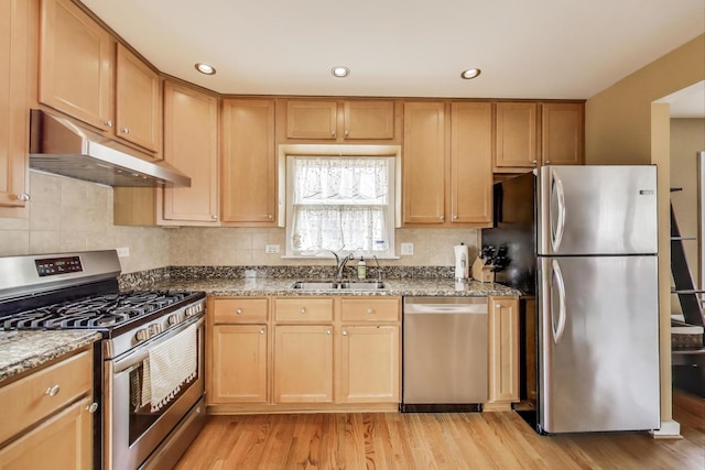 kitchen featuring dark stone counters, a sink, appliances with stainless steel finishes, light wood-style flooring, and under cabinet range hood