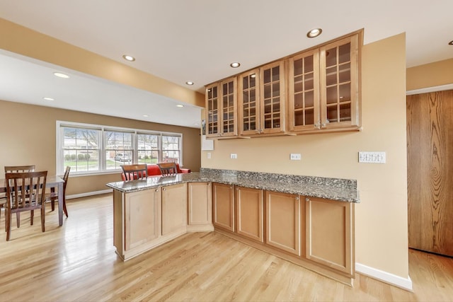 kitchen with light wood finished floors, a peninsula, stone counters, and glass insert cabinets