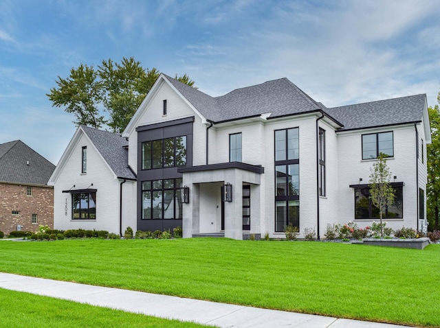 modern farmhouse with brick siding, a shingled roof, and a front lawn
