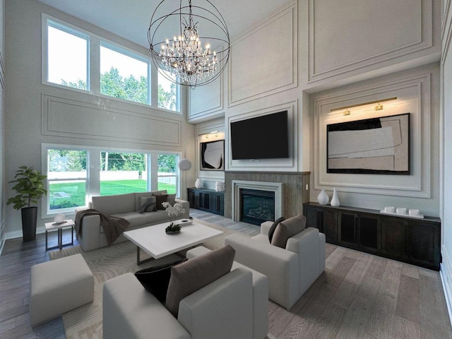 living room featuring a high ceiling, wood finished floors, a decorative wall, a glass covered fireplace, and a notable chandelier