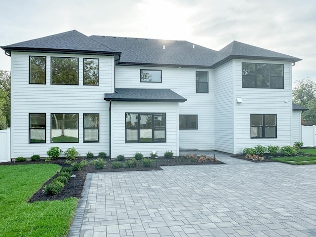 view of front of home featuring fence, a patio area, a front lawn, and roof with shingles