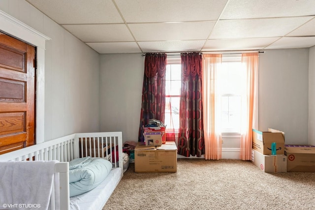 bedroom featuring carpet floors, a drop ceiling, and a crib