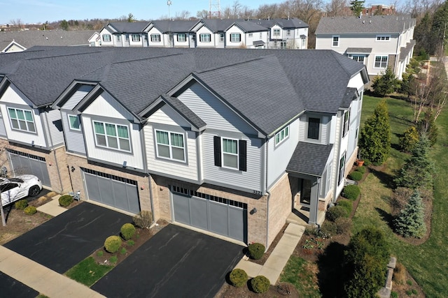 view of front of house with a shingled roof, a residential view, driveway, brick siding, and a garage