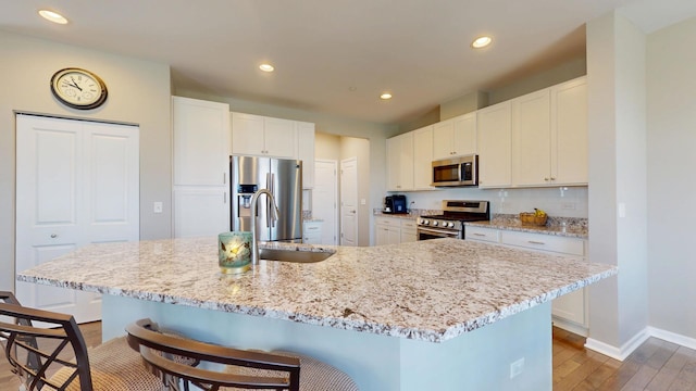 kitchen with stainless steel appliances, a sink, light wood-type flooring, recessed lighting, and a breakfast bar