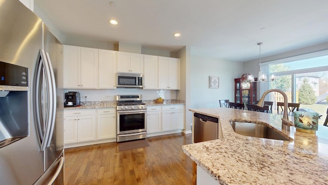 kitchen with stainless steel appliances, a sink, light wood-type flooring, pendant lighting, and a chandelier
