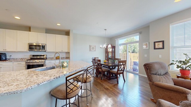 kitchen featuring white cabinets, a kitchen breakfast bar, a sink, appliances with stainless steel finishes, and hardwood / wood-style flooring