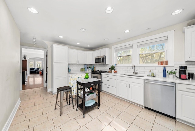 kitchen with white cabinets, stainless steel appliances, light countertops, a sink, and decorative backsplash