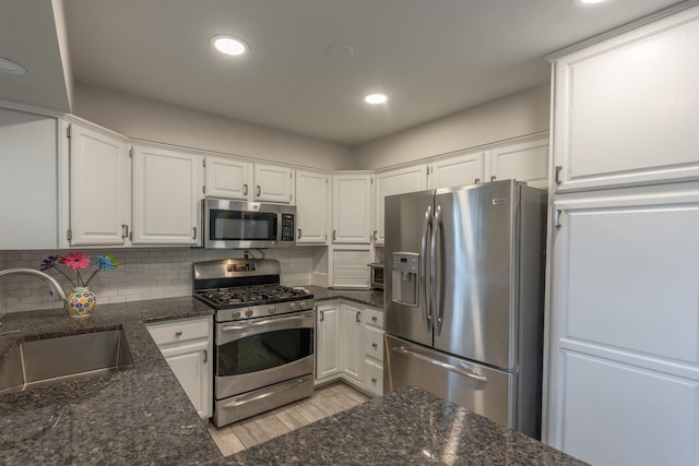 kitchen with dark stone counters, a sink, appliances with stainless steel finishes, and white cabinetry