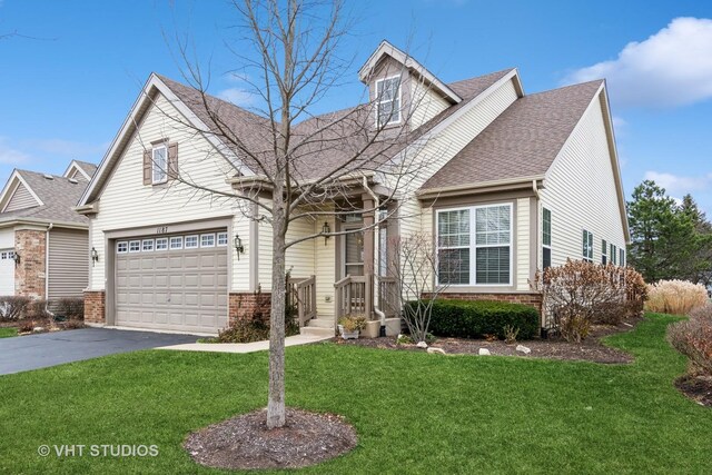 view of front of house with a front lawn, aphalt driveway, an attached garage, brick siding, and roof with shingles