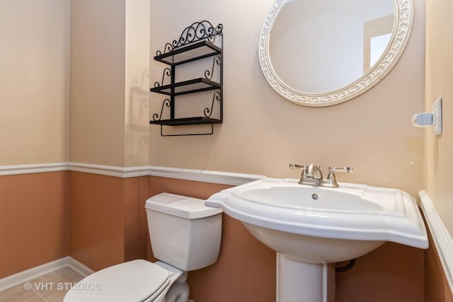 half bath with tile patterned floors, toilet, baseboards, and a sink