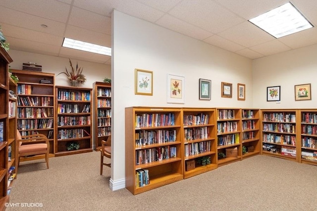 living area with bookshelves, carpet floors, and a drop ceiling