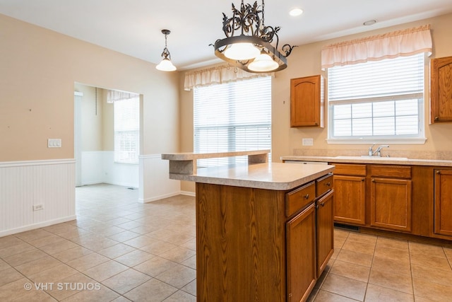 kitchen with brown cabinets, plenty of natural light, light countertops, a sink, and wainscoting