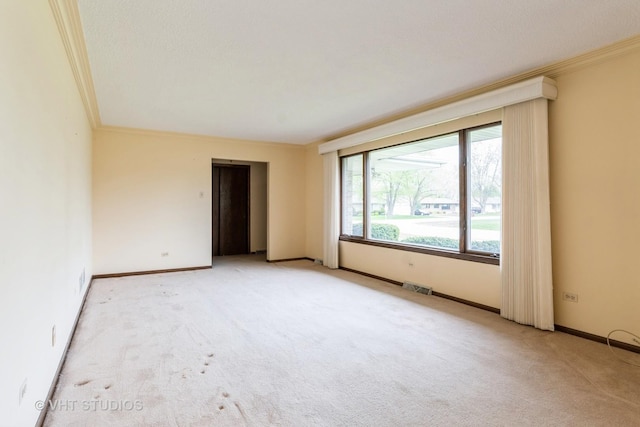 empty room featuring light colored carpet, baseboards, visible vents, and ornamental molding