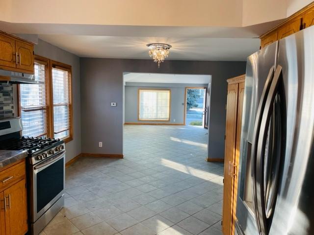 1218 Highland Ave, Joliet, IL 60435 - kitchen with dark countertops, brown cabinetry, stainless steel appliances, baseboards, and under cabinet range hood