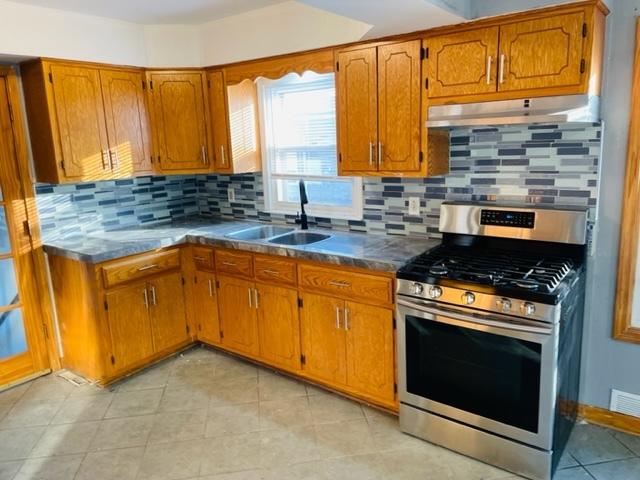 1218 Highland Ave, Joliet, IL 60435 - kitchen featuring brown cabinetry, under cabinet range hood, a sink, and stainless steel gas range oven