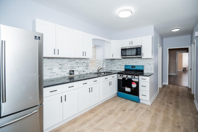 kitchen featuring a sink, light wood-style floors, white cabinetry, backsplash, and appliances with stainless steel finishes